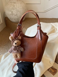 Brown vintage leather bucket bag with top handles, adjustable strap and cute bear charm