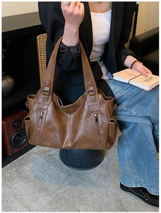 Close-up of brown vintage leather tote bag featuring decorative metal zippers and side pocket