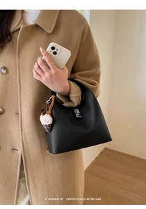 Detail of black lychee grain leather bucket bag with silver lock and plush charm