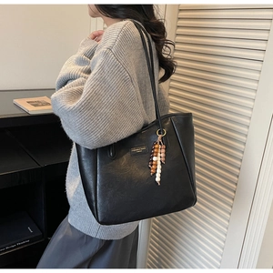 Detail of black large capacity tote bag featuring a leather texture and beaded tassel charm