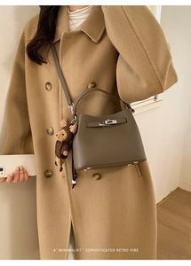 Detail of taupe bucket bag with metal lock, pebble leather texture and mini bear charm