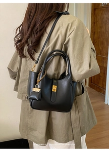 Detail of a black leather bucket bag featuring a gold twist lock and a mini hanging pouch
