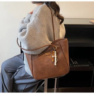 Detail of retro brown tote bag with beaded pendant and fashion logo on leather