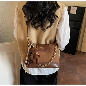 Detail of a brown quilted leather crossbody bag with gold chain and plush bear charm