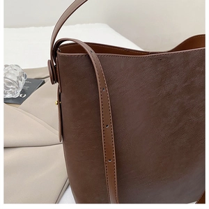Close-up of brown textured leather bucket bag with adjustable shoulder strap and metal buckle