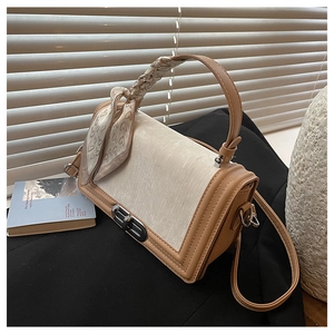 Detail einer braunen Kontrasttasche mit Metalldrehverschluss und Seidenschal-Dekoration