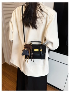 Detail of black crossbody bag featuring mixed textures and a cute brown bear charm