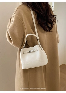 Detail of white lychee leather bucket bag with silver twist lock on camel wool coat