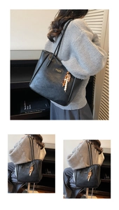 Detail of black faux leather tote with textured finish and wooden bead charm on shoulder strap