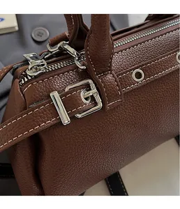 Close-up of brown lychee-textured leather bag with silver metal buckles and white stitching