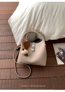 Detail of beige lychee leather bucket bag with silver twist lock and heart pendant