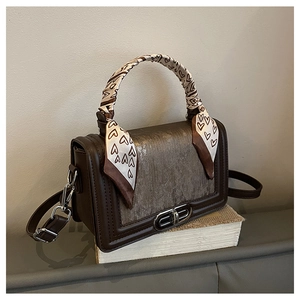 Details einer braunen Ledertasche mit Metallic-Klappe und verzierten Herz-Seidenschal