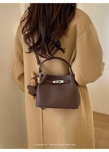 Detail of dark brown leather bucket bag with silver metal lock and teddy bear charm