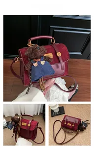 Detail of burgundy patchwork crossbody bag featuring a plush teddy bear charm accessory