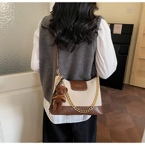 Detail of a color-block quilted shoulder bag with golden chain and plush bear charm