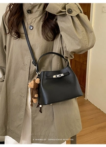 Detailed view of black litchi pattern leather bucket bag with silver twist lock and bear charm
