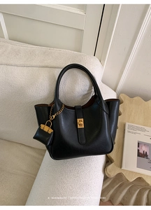 Detail of black lychee grain tote with gold clasp and mini charm on a white sofa