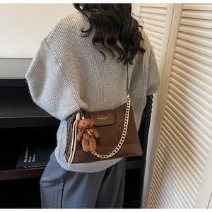 Detail of dark brown leather bag with gold chain and plush bear charm on a model