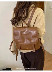 Dettaglio di uno zaino vintage in pelle marrone con logo in metallo dorato e fibbie