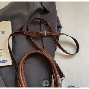 Detail of brown litchi leather bag showing white stitching and silver buckle on strap