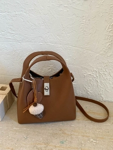 Brown lychee leather bucket bag with top handles, crossbody strap and plush charm
