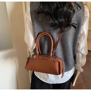 Detail of a brown leather baguette bag with silver buckles worn as a crossbody bag
