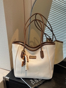 Large beige leather tote bag with brown trim and wooden bead charm for daily commute