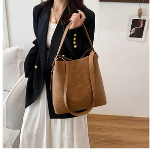 Close-up of caramel PU leather bucket bag with wide strap on shoulder of a woman