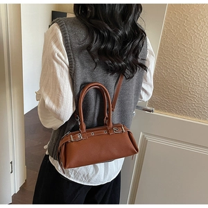Detail view of a brown pebbled leather baguette bag worn over the shoulder by a model