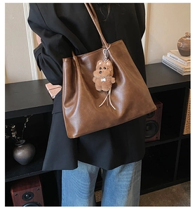 Detailansicht der braunen PU-Leder-Tote-Bag mit Plüschbären-Anhänger in schickem Ambiente
