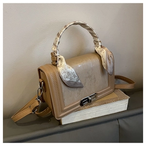 Detail der beigen Handtasche mit silbernem Drehverschluss und Herzmuster-Seidenschal