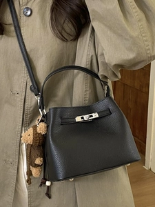 Black litchi leather bucket bag with metal turn-lock and cute bear charm on a model