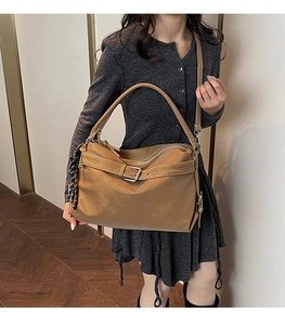 Brown leather tote bag with buckle detail and woven tassel shown on shoulder