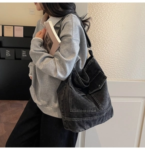 Detail of a large black denim tote bag with contrast stitching and front pockets
