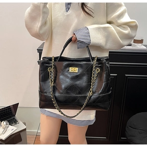 Detail of black quilted tote bag featuring glossy finish, chain strap and gold twist lock