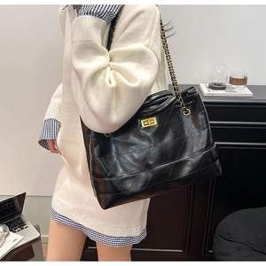Detail of black quilted tote bag with golden metal chain strap and square turn-lock closure