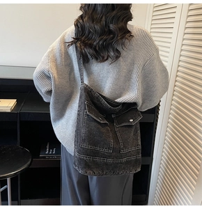 Detail view of charcoal gray denim crossbody tote with dual pockets on gray knit sweater