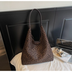 Sac fourre-tout à motif léopard avec ordinateur et livre sur un lit blanc
