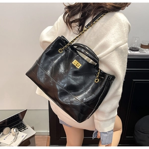Detail of black quilted leather tote bag with gold chain strap and turn-lock closure