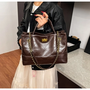Detail view of large brown quilted tote bag with golden metal twist lock and chain strap