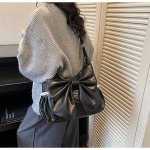 Detail of black tote bag with oversized bow and white lace trim on faux leather
