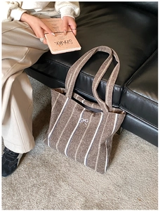 Close-up of vertical striped knit tote bag with a small silver bow detail in a cozy setting