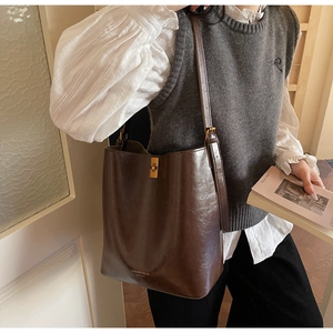 Close-up of a vintage dark brown leather bucket bag with metallic twist-lock on a model