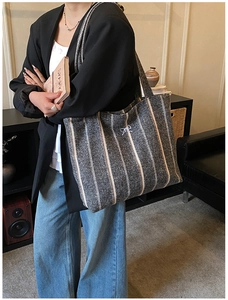 Detailed view of large grey striped canvas tote bag with bow detail worn over the shoulder