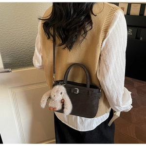 Retro dark brown bucket bag with plush rabbit charm worn cross-body style on sweater