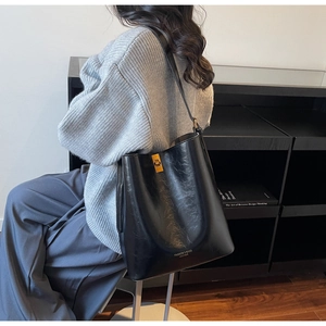 Detail of black glossy bucket bag featuring gold metal lock and elegant fashion text logo