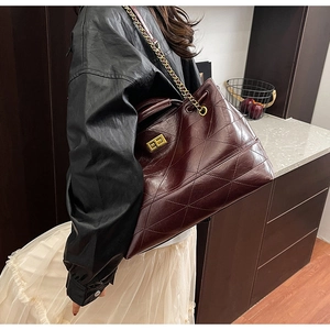 Detail of red-brown quilted leather tote bag with gold chain strap and square metal lock
