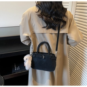 Detail of black suede bucket bag with leather buckle and plush bunny charm on trench coat