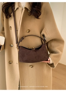 Détail du sac à main en daim marron foncé avec boucle dorée sur manteau de laine