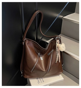 Detail of dark brown leather tote bag with decorative zippers and plush bear charm